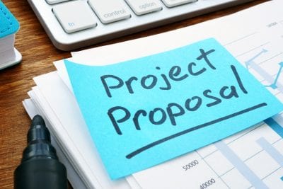 Project Proposal with stack of documents and keyboard.